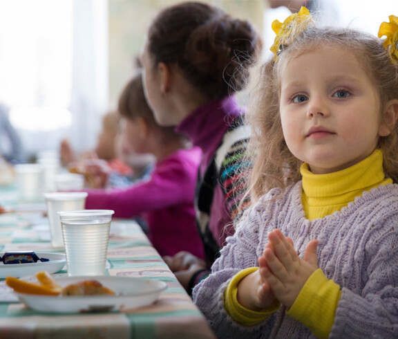 bunt gekleidete Kinder sitzen gemeinsam beim Essen 