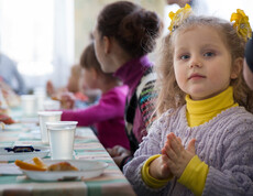 bunt gekleidete Kinder sitzen gemeinsam beim Essen 