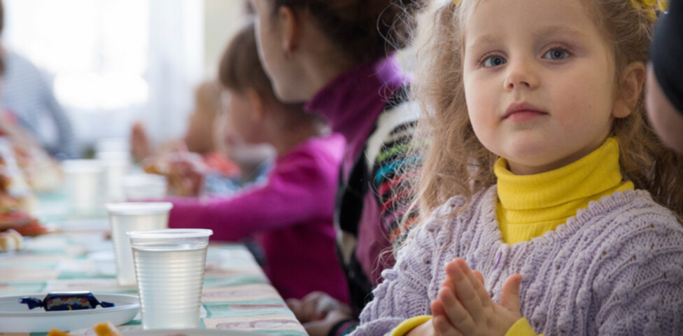 bunt gekleidete Kinder sitzen gemeinsam beim Essen 