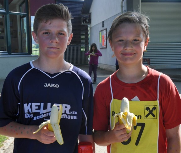 Zwei Buben in Lauftrikots essen Bananen.