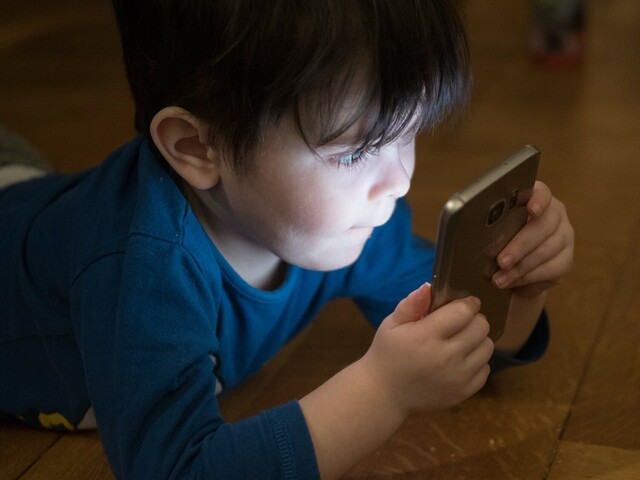 Man sieht einen Bub, er hält ein Handy in der Hand und schaut hinein.