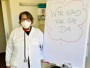Ärztin mit Schutzmaske in der Marienambulanz neben Infoschild