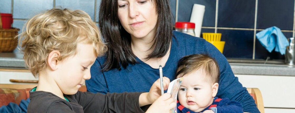 Eine Mutter sitzt mit ihren zwei Kindern an einem Küchentisch.