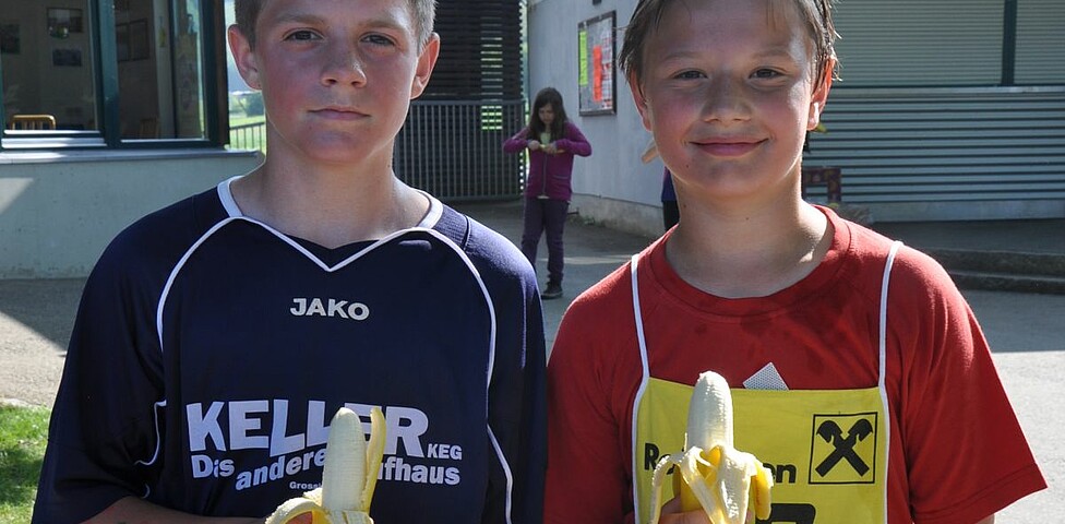 Zwei Buben in Lauftrikots essen Bananen.